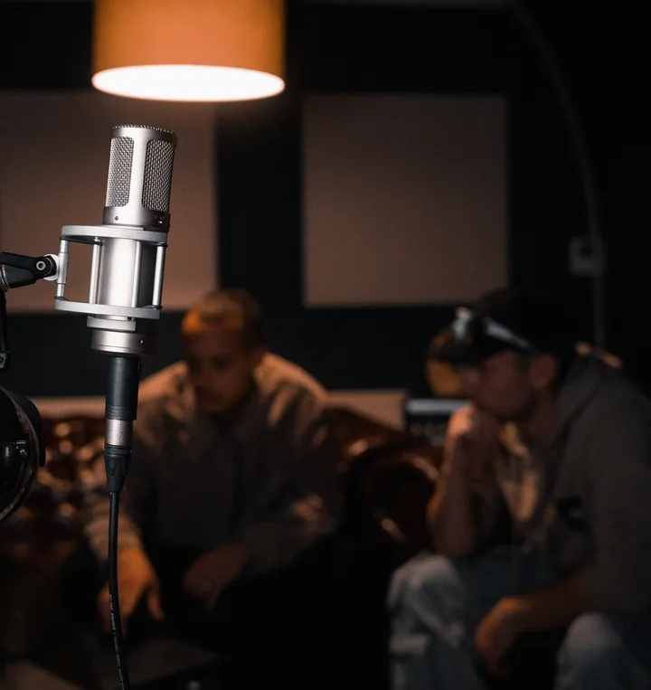 Großmembran-Mikrofon im Studio, im Hintergrund zwei Personen auf dem Sofa